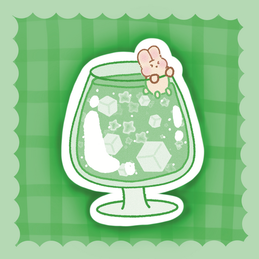 A cute die-cut sticker featuring a green cocktail glass filled with white ice cubes and a small pink bunny character sitting on the rim, set against a green plaid background with a scalloped border.
